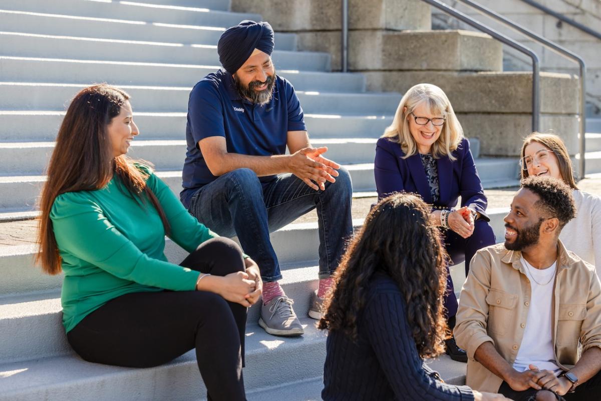 GoDaddy CEO Aman Bhutani seated with a small group of people on steps.